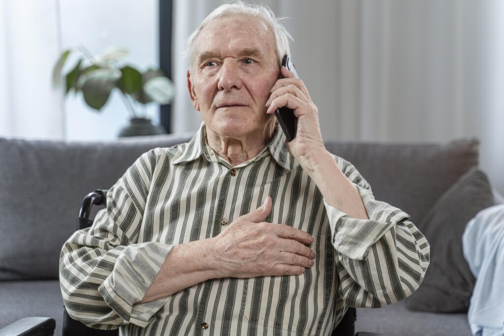 Sijedi umirovljenik telefonira s dlanom na prsima.