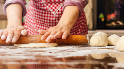 Žena sa crvenom pregačom valjkom za tijesto valja tijesto