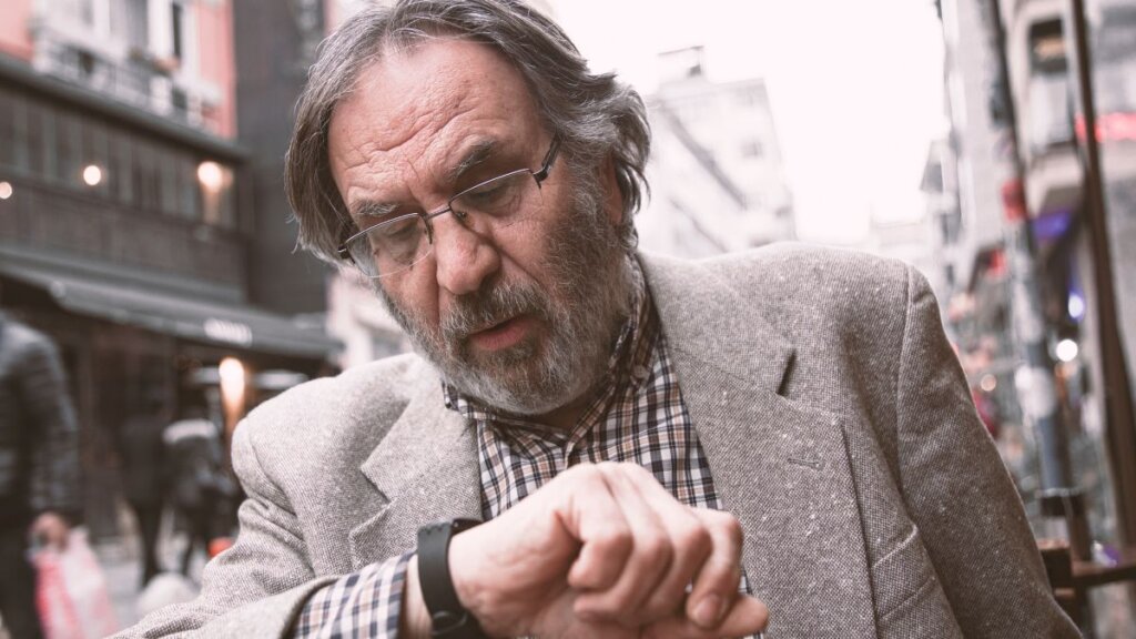 Umirovljenik u kariranoj košulji i sivom sakou provjerava koliko je sat na njeovom ručnom satu