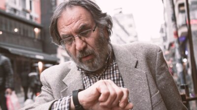 Umirovljenik u kariranoj košulji i sivom sakou provjerava koliko je sat na njeovom ručnom satu