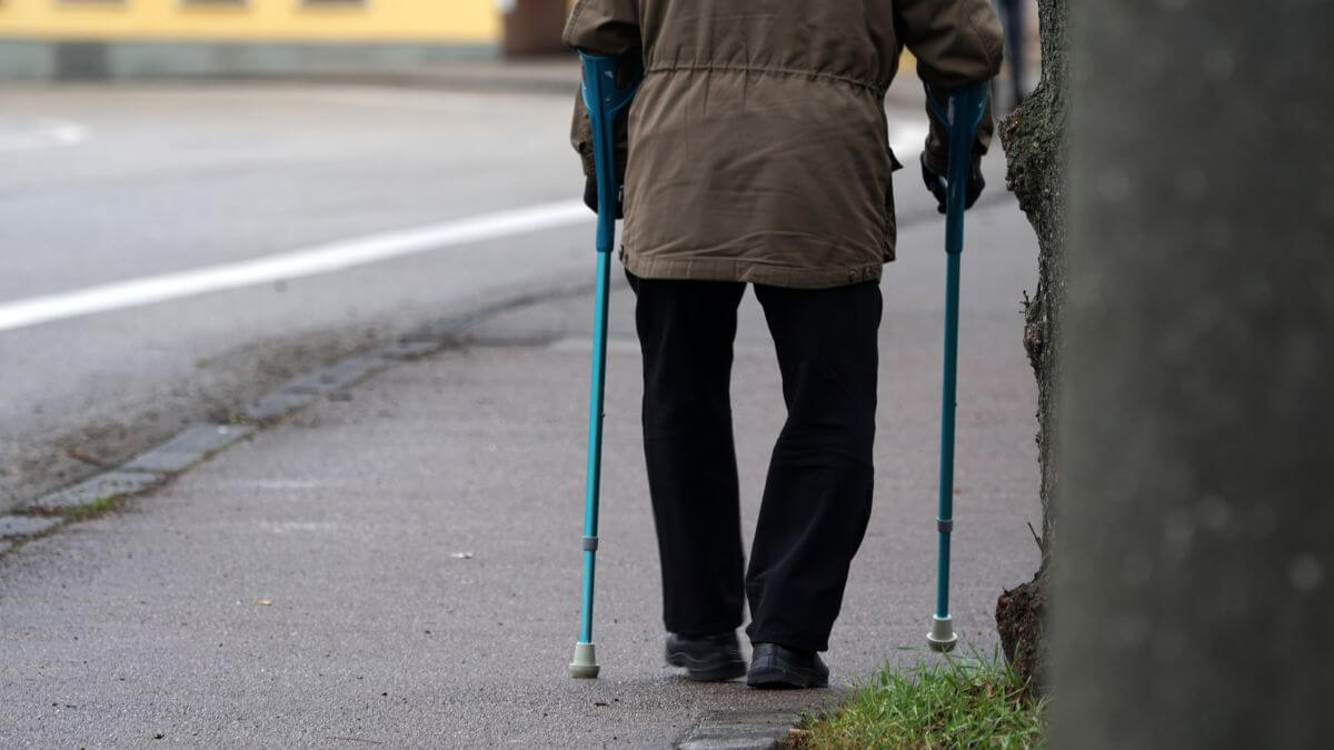 stariji muškarac okrenut leđima na štakama šeće ulicom