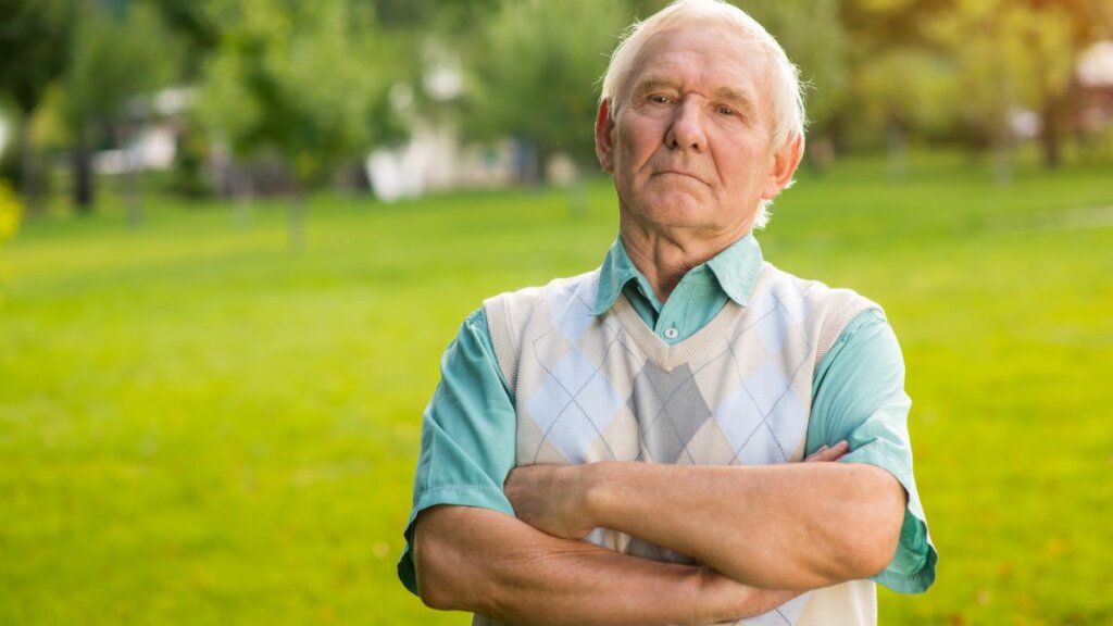 Nezadovoljan umirovljenik u košulji kratkih rukava i pletenom prsluku na livadi