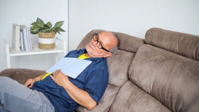 Umirovljenik drijema na kauču s knjigom na prsima