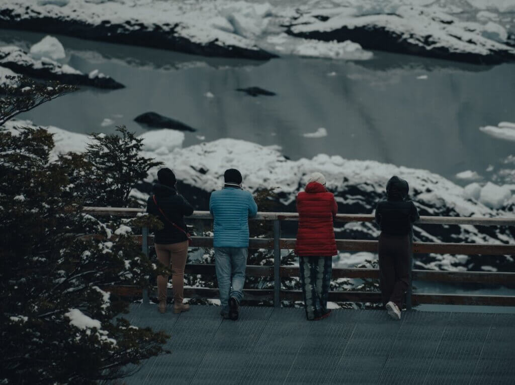 četiri osobe naslonjene na ogradu i gledaju zaleđenu rijeku okruženu snijegom